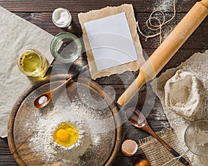 Ingredients for cooking dough or bread. Broken egg on top of a bunch of white rye flour. Dark wooden background.