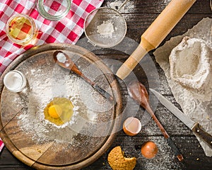 Ingredients for cooking dough or bread. Broken egg on top of a bunch of white rye flour. Dark wooden background.