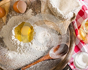 Ingredients for cooking dough or bread. Broken egg on top of a bunch of white rye flour. Dark wooden background.