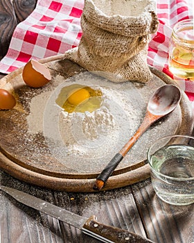 Ingredients for cooking dough or bread. Broken egg on top of a bunch of white rye flour. Dark wooden background.