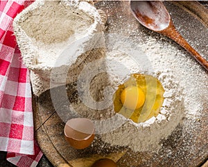 Ingredients for cooking dough or bread. Broken egg on top of a bunch of white rye flour. Dark wooden background.