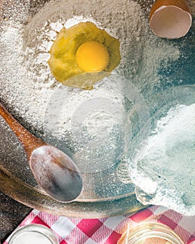 Ingredients for cooking dough or bread. Broken egg on top of a bunch of white rye flour. Dark wooden background.