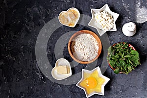 Ingredients for cooking gnocchi or dumplings with nettle on a dark gray concrete background: ricotta cheese, fresh nettle, egg,