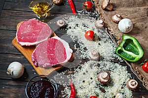 Ingredients for cooking healthy meat dinner. Raw uncooked beef rib eye steaks with mushrooms, rice, herbs and spices on table back