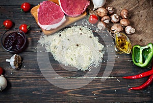 Ingredients for cooking healthy meat dinner. Raw uncooked beef rib eye steaks with mushrooms, rice, herbs and spices on table back