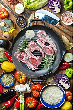Ingredients for cooking healthy meat dinner. Raw uncooked lamb chops in iron grill pan with vegetables, rice, herbs and