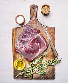 Ingredients for cooking meat raw steak with rosemary, pepper, spices and oil on a rustic wooden background