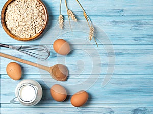 Ingredients for cooking, milk, eggs, oats and kitchenware on blue wooden background, top view