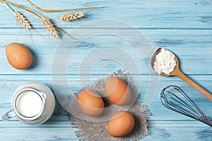 Ingredients for cooking, milk, eggs, wheat flour and kitchenware on blue wooden background, top view