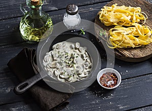 Ingredients for cooking pasta with creamy mushroom sauce - dry pasta, mushroom cream sauce, olive oil and spices. On a dark wooden