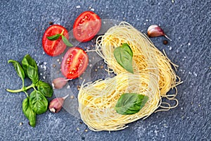 Ingredients for cooking pasta. Italian tagliatelle pasta with tomato on black wooden background.