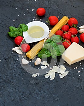 Ingredients for cooking pasta. Spaghetti, olive oil, garlic, Parmesan cheese, tomatoes and fresh basil on black slate