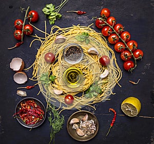 Ingredients for cooking pasta with tomato on a branch, oil, garlic and pepper, egg on wooden rustic background top view close up