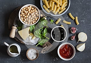 Ingredients for cooking rigatoni pasta with chickpeas, spinach and olives in a tomato sauce on a dark background, top view.