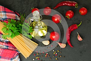 Ingredients for cooking spaghetti - raw spaghetti, cherry tomatoes, chili peppers, garlic, herbs, spices and olive oil on a black