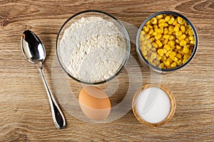 Ingredients for corn pancakes. Bowl with flour, jar of corn, egg, salt on wooden table. Top view