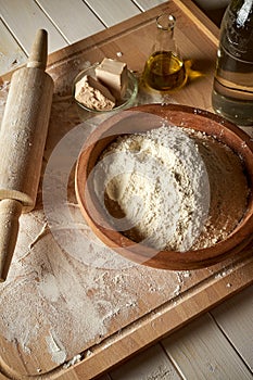 Ingredients for dough on pastry board with flour and rolling pin on table