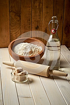 Ingredients for dough on pastry board with flour and rolling pin on table