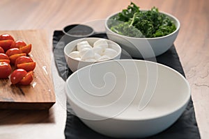 Ingredients and empty white bowl on walnut table