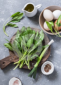 Ingredients for green shakshuka - fresh spinach, garlic, ramson and organic farm eggs on grey background