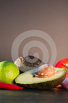 Ingredients for guacamole, avocado, lime, onion, garlic, tomato, pepper on dark wooden background, free space