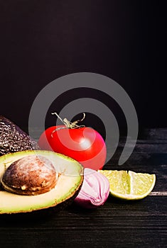 Ingredients for guacamole, avocado, lime, onion, garlic, tomato, pepper on dark wooden background, free space