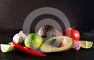 Ingredients for guacamole, avocado, lime, onion, garlic, tomato, pepper on dark wooden background, free space