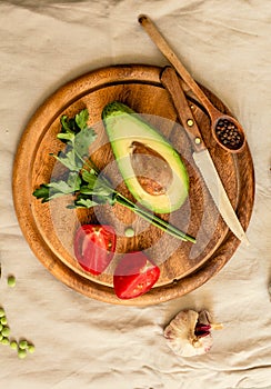 Ingredients for guacamole on a wooden board. Parsley, avocado, tomatoes, garlic, black pepper