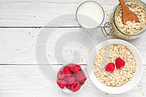 Ingredients for healthy breakfast - miilk, raspberries and oat muesli on white wooden table. top view