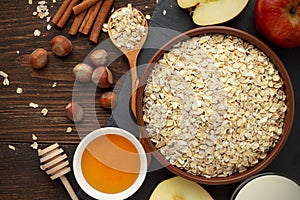 Ingredients for healthy breakfast: rolled oat flakes, milk, honey, hazelnut, cinnamon on dark rustic wooden table.