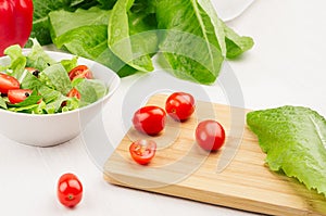 Ingredients for healthy vegetarian spring salad - fresh greens, tomatoes, pepper on cuttingboard on white wood background, close