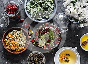 Ingredients for herbal tea - currant, mint, raspberry leaves, chamomile and calendula flowers, rose hips and teapot on a dark