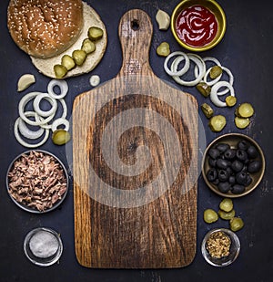 Ingredients for homemade burger with tuna, laid out around a cutting board on wooden rustic background top view border, place for