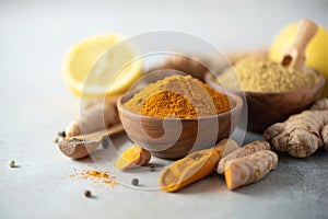Ingredients for hot ayurvedic drink. Turmeric powder, curcuma root, cinnamon, ginger, lemon over grey background. Copy