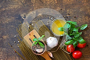 Ingredients for italy cuisine. Spinach spaghetti, herbs, spices, olive oil and tomatoes on a rustic table. Top view.