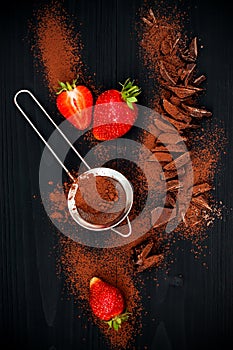 Ingredients for making chocolate brownies. Strawberries, chopped chocolate with cocoa over black wooden background, top view.