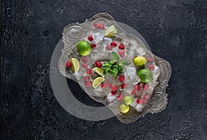 Ingredients for making lemonade Ice cubes, raspberry, lime, lemon and mint, served on old tray over dark rustic