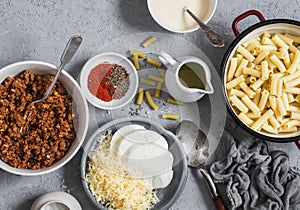 Ingredients for making mac and cheese. Pasta, cheese, meat tomato sauce on a gray background, top view.