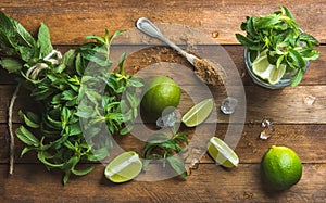 Ingredients for making mojito summer cocktail. Fresh mint bunch and leaves, limes, spoon of brown sugar, ice over rustic