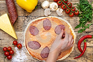 Ingredients for making pizza, before baking, on a wooden table, top view of the hand laid out sausage, step-by-step recipe