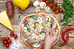 Ingredients for making pizza, before baking, on a wooden table, top view hand pours grated cheese, step-by-step recipe