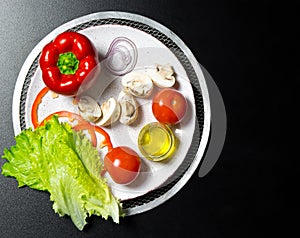 Ingredients for making pizza. Mushrooms, tomatoes, pepper, salt, herbs, oil, onions on a plate on a black concrete background.The