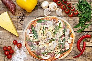 Ingredients for making pizza and raw pizza before baking, on a wooden table, top view, step-by-step recipe