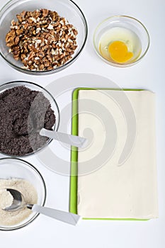 Ingredients for making puff pastry curls stuffed with poppy and walnut. Are laid out on a white table top