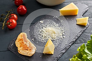 Ingredients for making salad. Piece and grated parmesan cheese on black serving board, cherry tomatoes