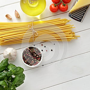 Ingredients for mediterranean pasta dish: bucatini or spaghetti, tomatoes, basil, spice on white wooden background.