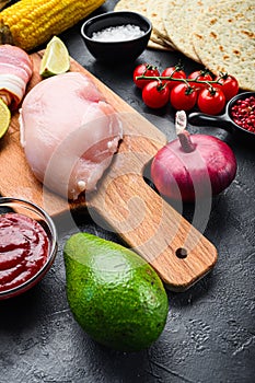 Ingredients for Mexican tacos with chicken meat, corn tortilla, salsa, chilli over black background, side view