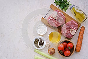 Ingredients for ossobuco, beef shank stew on a bone with carrots, tomatoes and celery on a light concrete background. Main meat