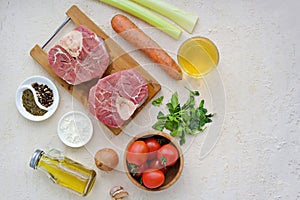 Ingredients for ossobuco, beef shank stew on a bone with carrots, tomatoes and celery on a light concrete background. Main meat