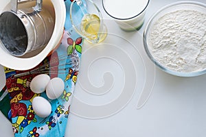 Raw ingredients for pancakes are laid out on a multi-colored tablecloth and white background and cpoy space photo